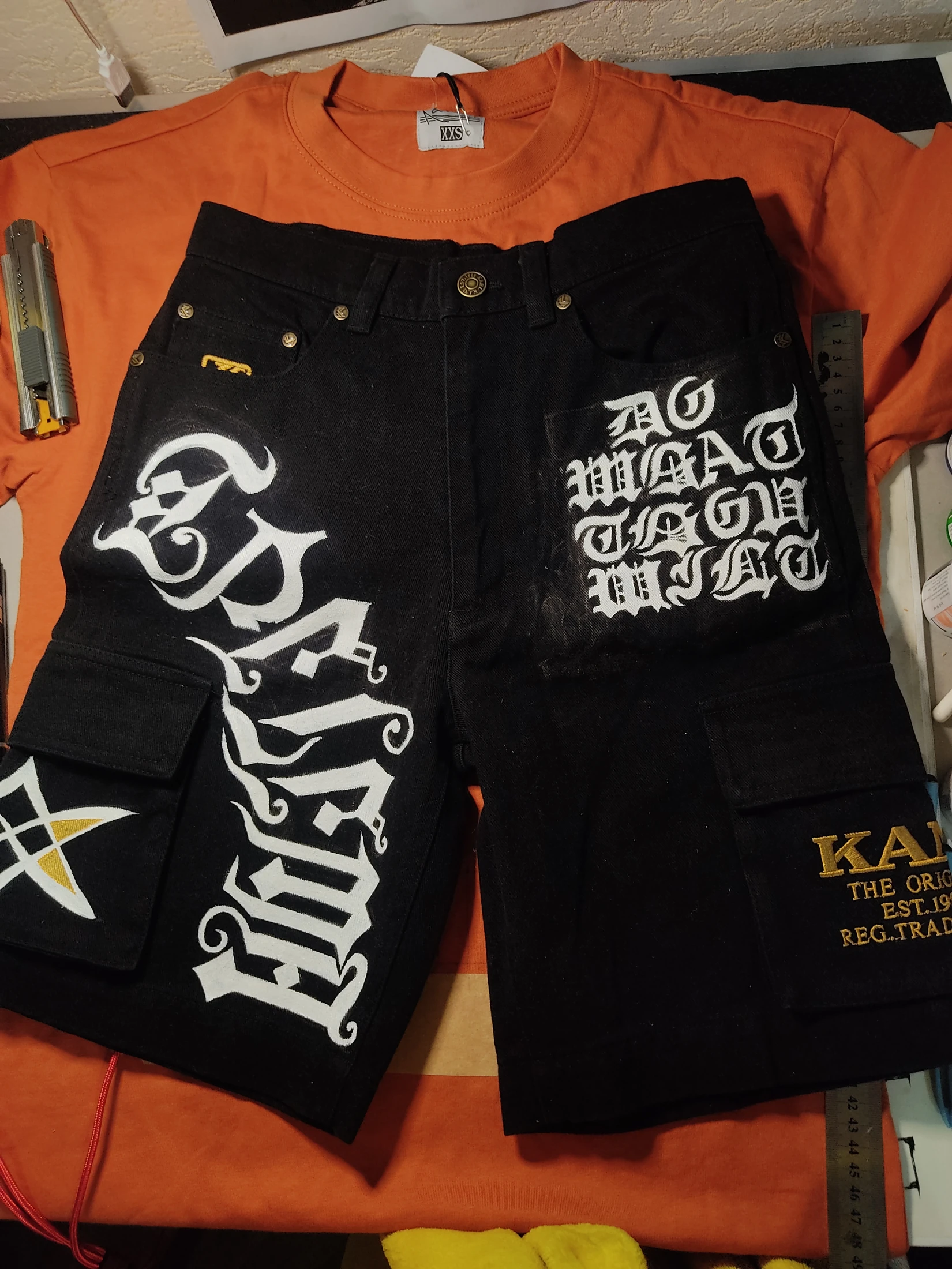 White Gothic lettering and a star motif across black cargo shorts. Photograph of the hand-painted piece.