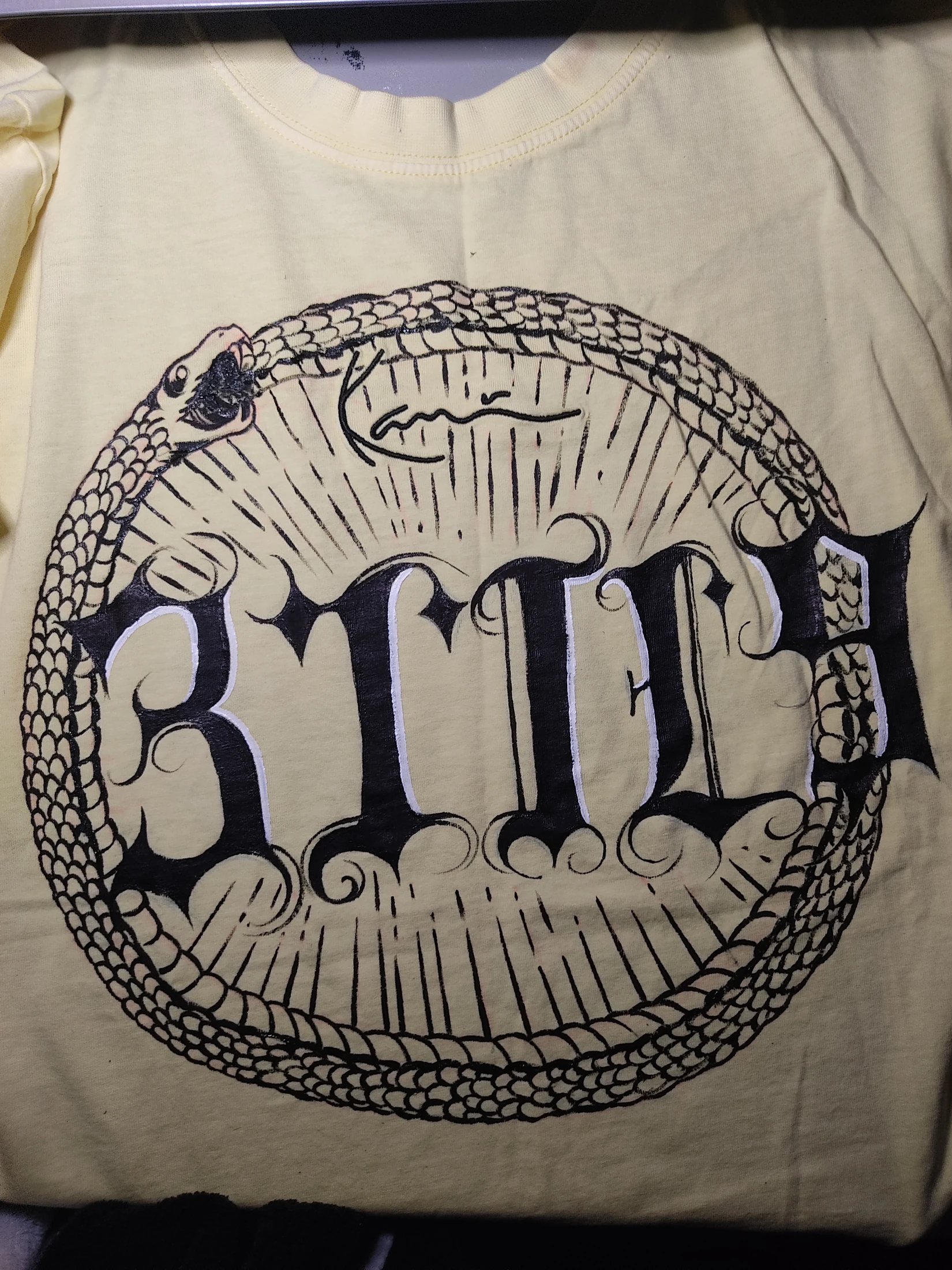 Black 3TIL9 lettering inside a scaled serpent circle with radiating lines. Photograph of the hand-painted piece.