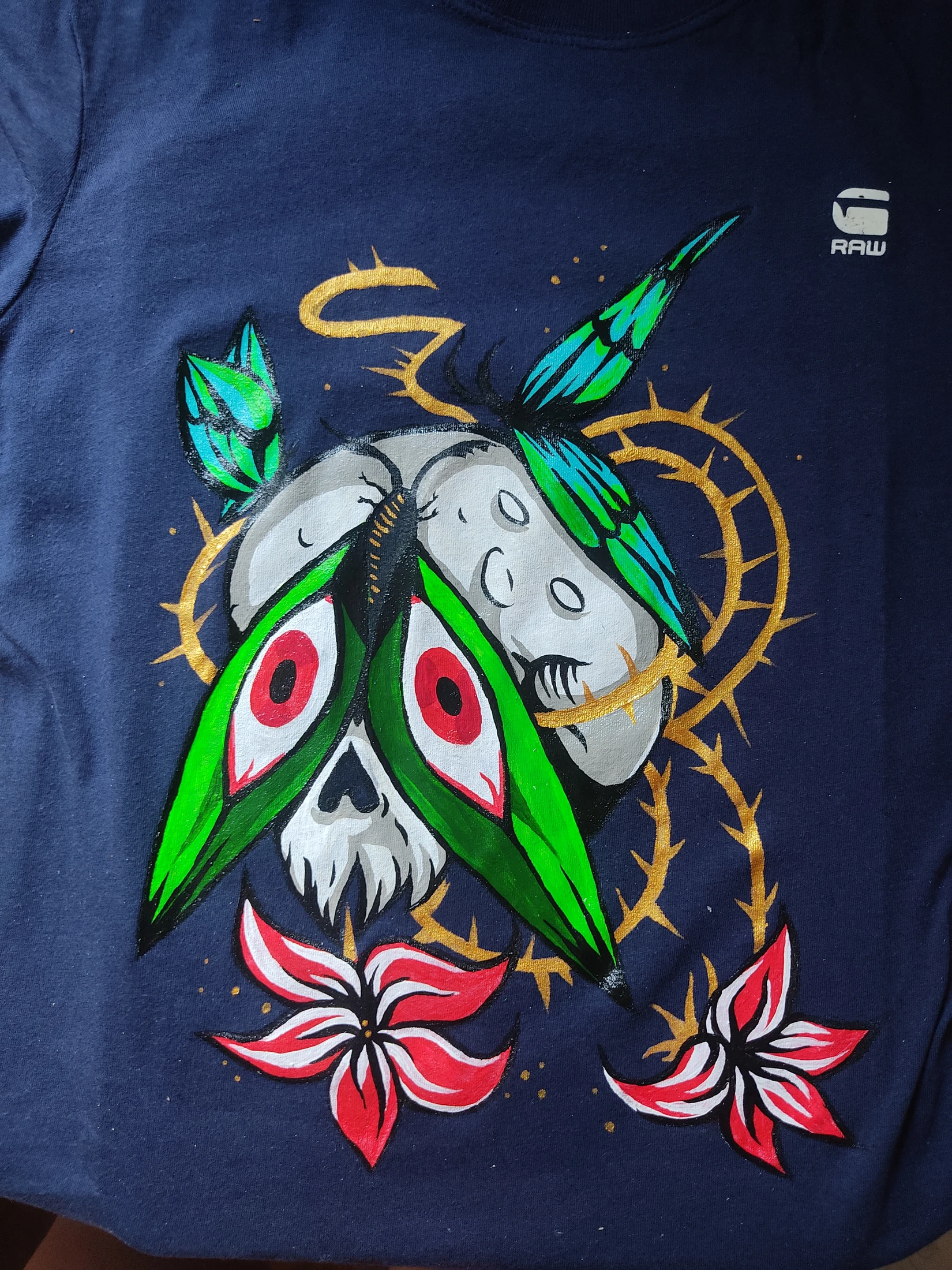 A skull-like moth with bright green wings, a pale moon, gold loops and red-and-white flowers. Photograph of the hand-painted piece.