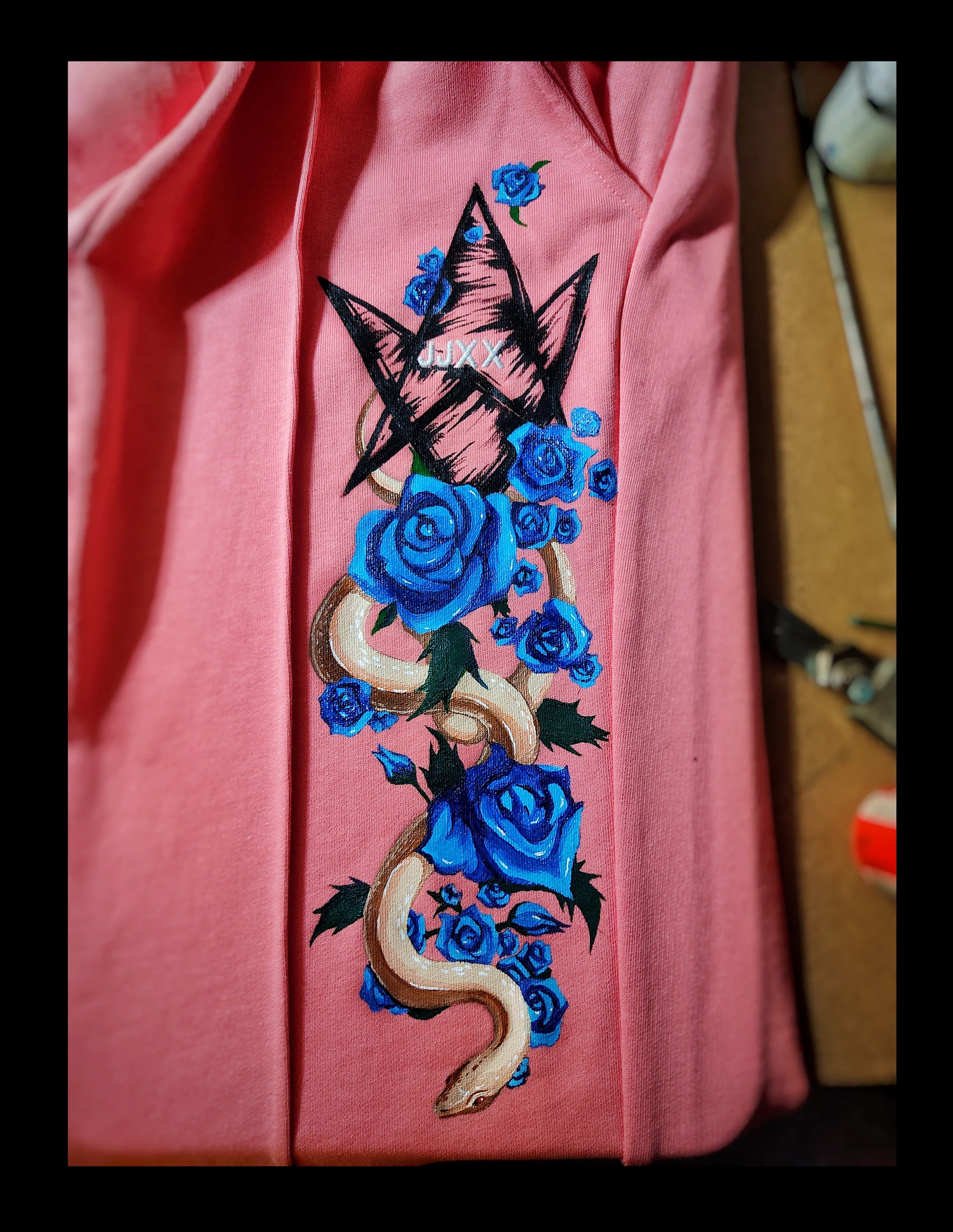 Blue roses and a pale snake beneath a black pentagram on pink. Photograph of the hand-painted piece.