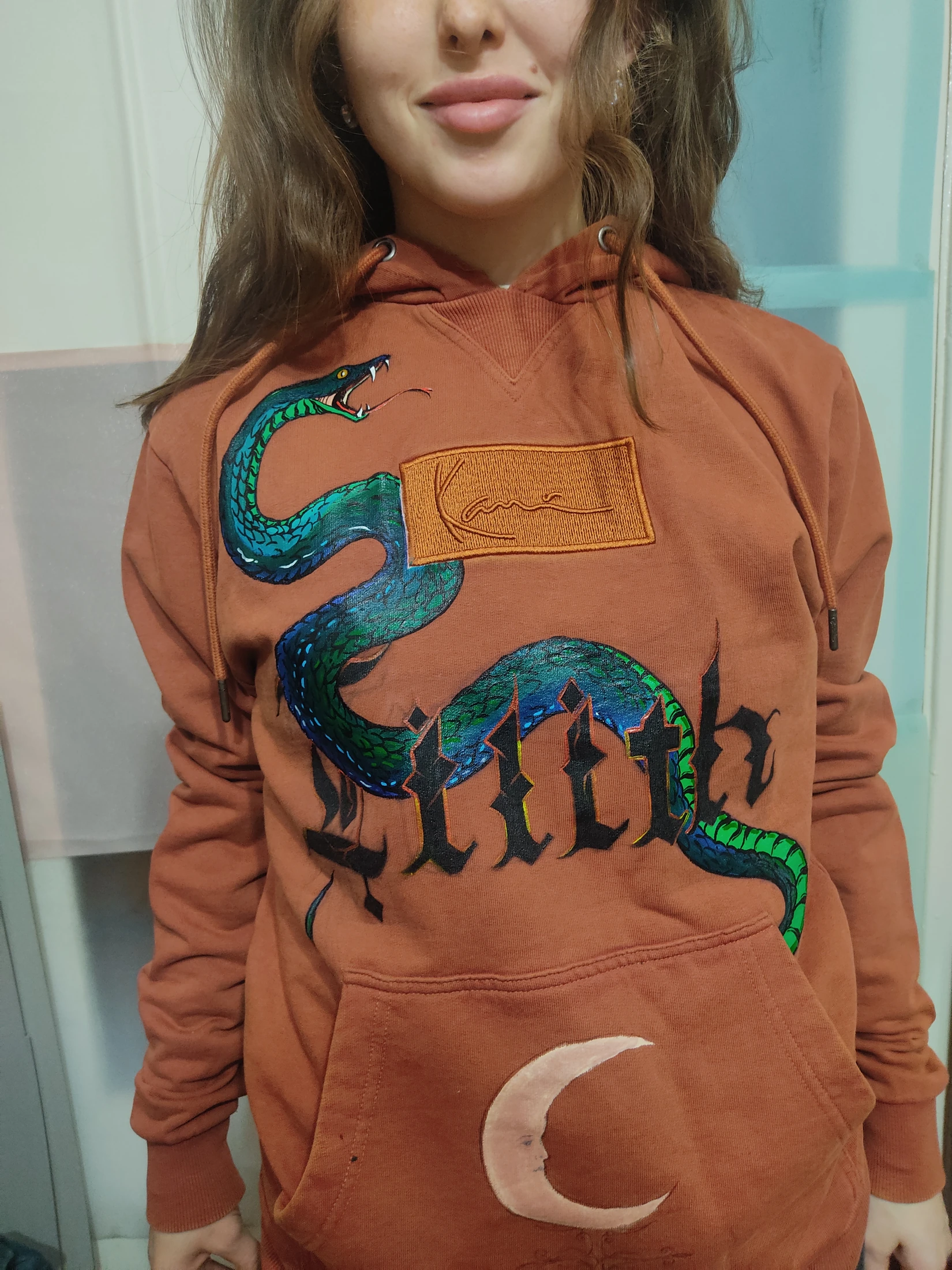 A blue-green snake crosses black Gothic lettering; a pale crescent sits on the front pocket. Photograph of the hand-painted piece.