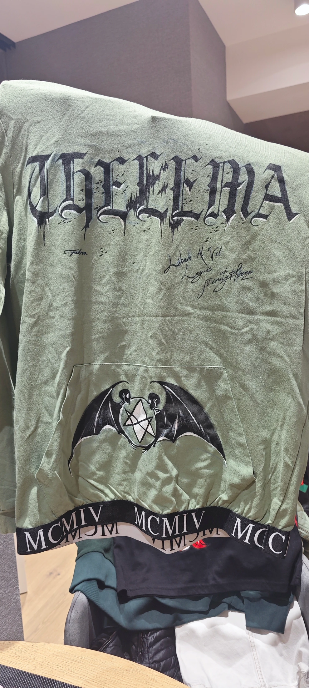 Black Thelema lettering above a winged star on the front pocket, with repeated Roman lettering along the hem. Photograph of the hand-painted piece.