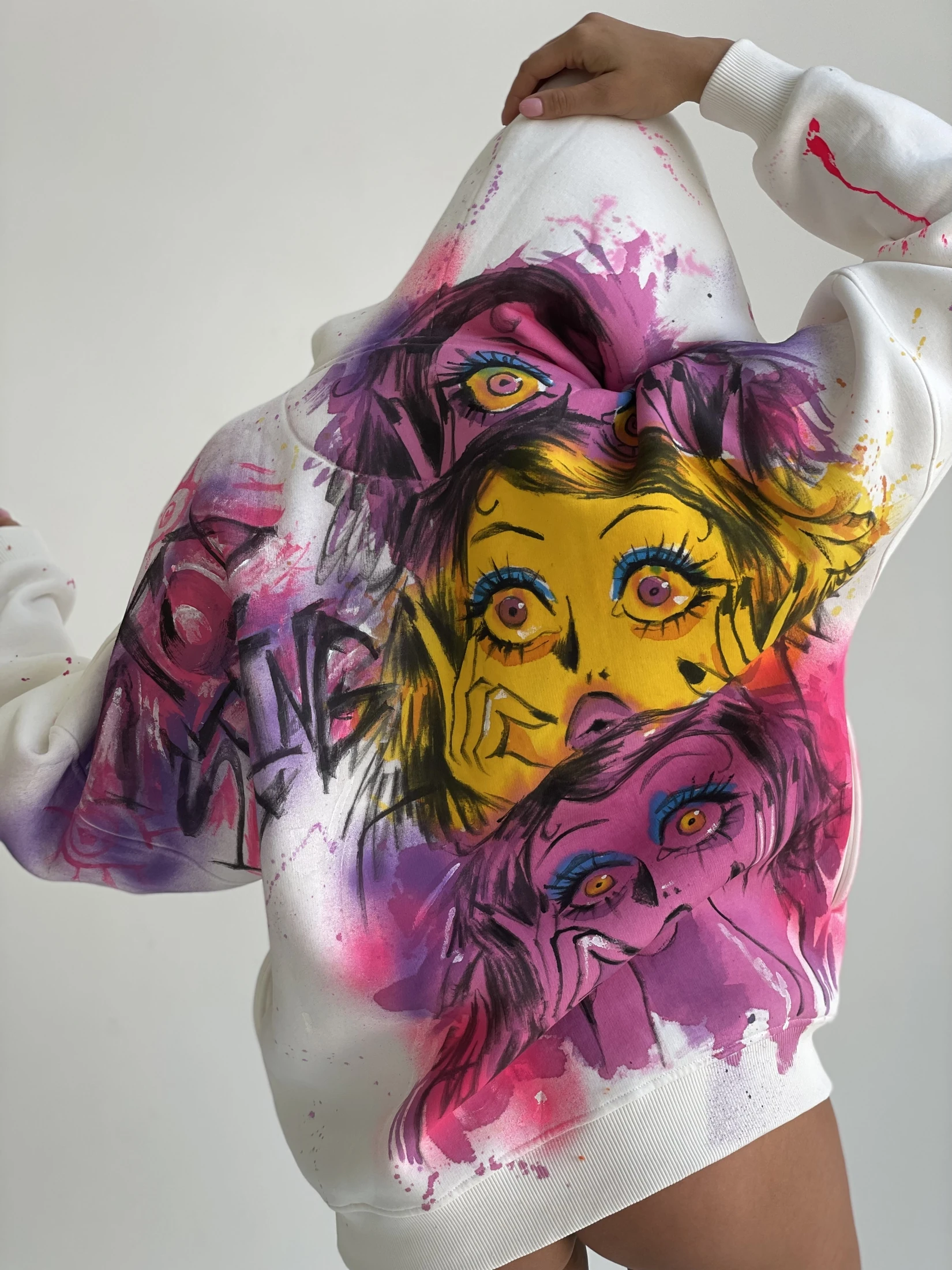 Large pink and yellow illustrated faces, blue eye accents and loose painted marks across white. Photograph of the hand-painted piece.